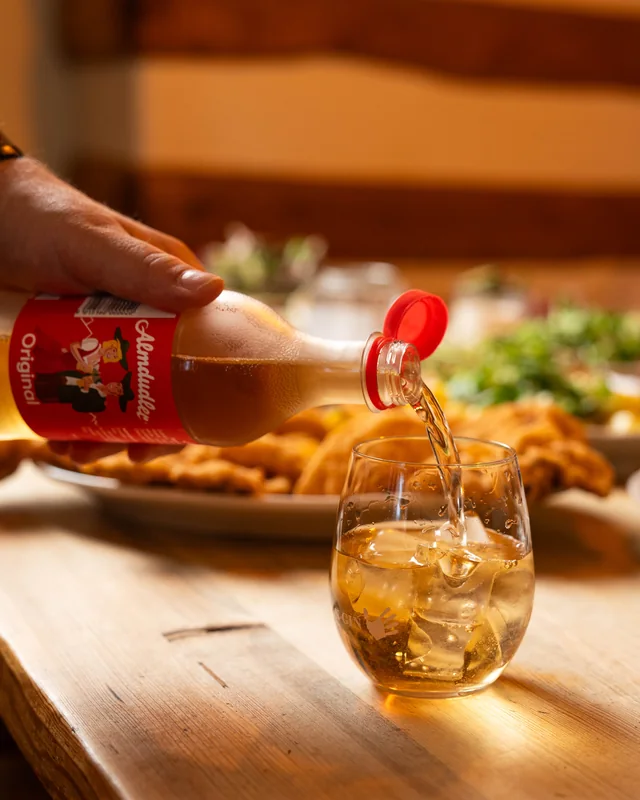 Almdudler hälls upp i ett glas med is bredvid ett fat schnitzlar