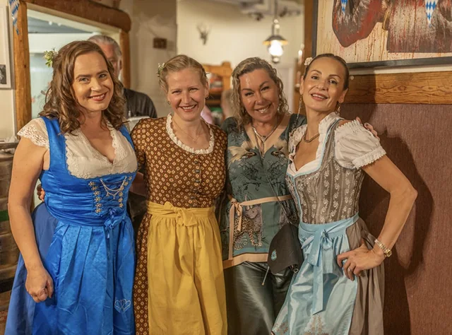 Fyra kvinnor i dirndl framför den skurna träpanelen i matsalen