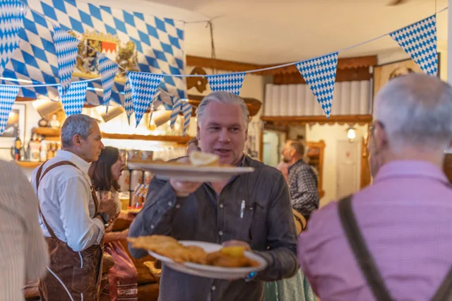 Matsalen under Oktoberfest med blåvit vimpelrad i taket och en kypare som bär två schnitzlar
